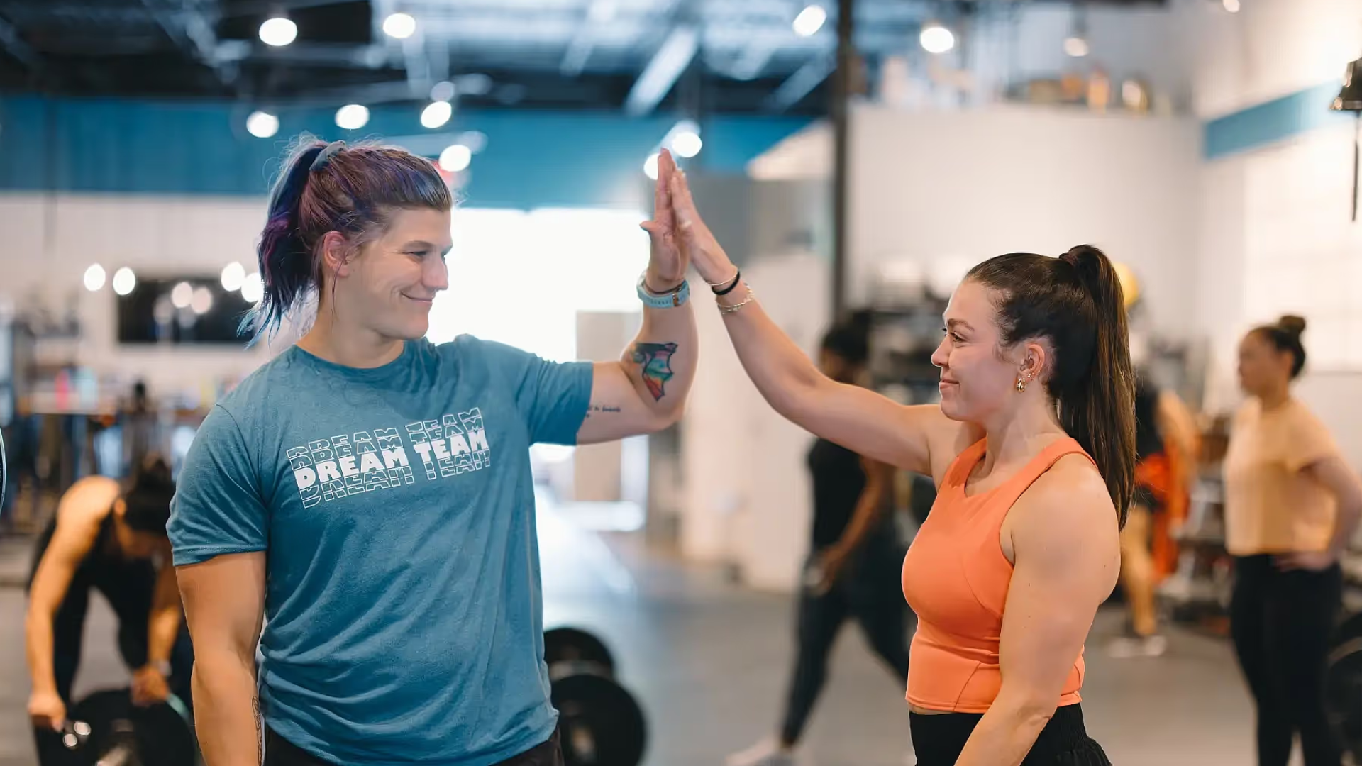 A female coach in a CrossFit gym in Atlanta, GA assists an athlete with a bar exercise, emphasizing proper form and technique.