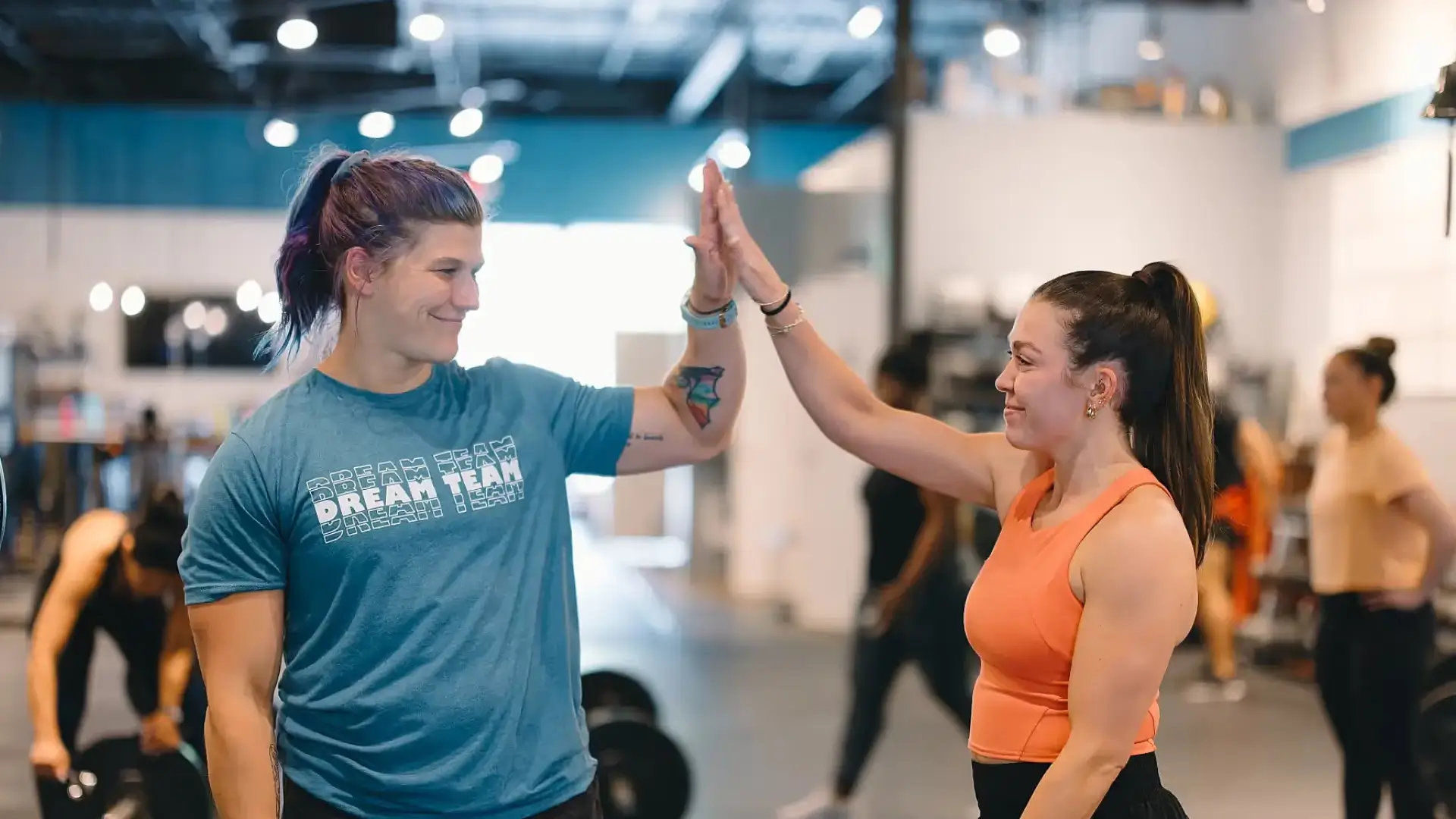 A female coach in a CrossFit gym in Atlanta, GA assists an athlete with a bar exercise, emphasizing proper form and technique.