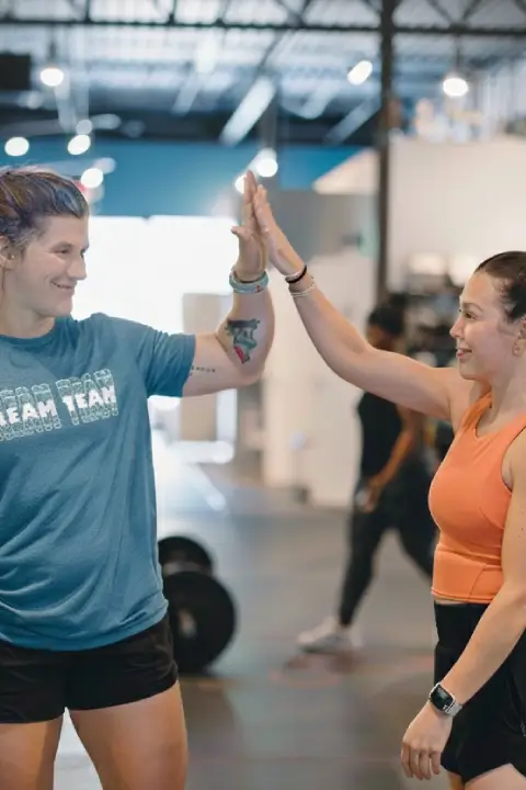 A female coach in a CrossFit gym in Atlanta, GA assists an athlete with a bar exercise, emphasizing proper form and technique.