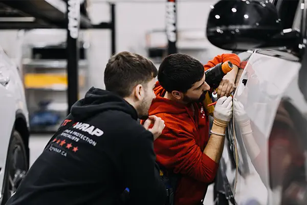 A Top Wrap Academy professional supervising a student vinyl wrapping a car