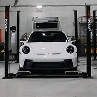 Front view of a white Porsche sports car positioned on a car lift inside a garage.