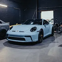 Light blue Porsche sports car parked indoors on polished floor beside other vehicles.