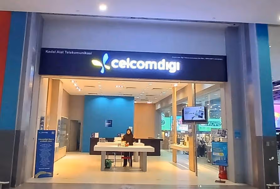CelcomDigi store at KLIA Terminal 2, featuring a modern retail setup with a staff member behind the counter and a prominent storefront sign in a shopping mall environment.