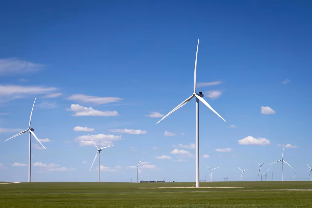 Meerdere witte windturbines op een groene vlakte tegen een blauwe lucht.