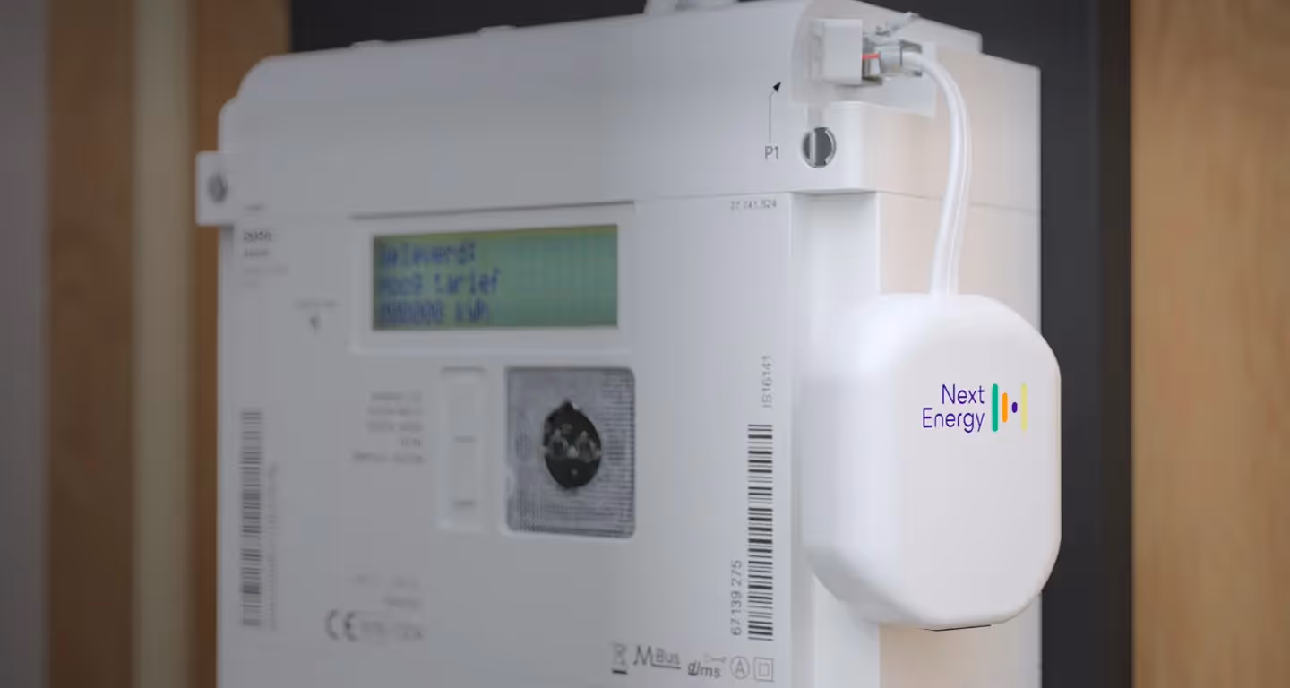 Een slimme meter in de meterkast. Aan de slimme meter hangt een witte dongle met het logo van NextEnergy.