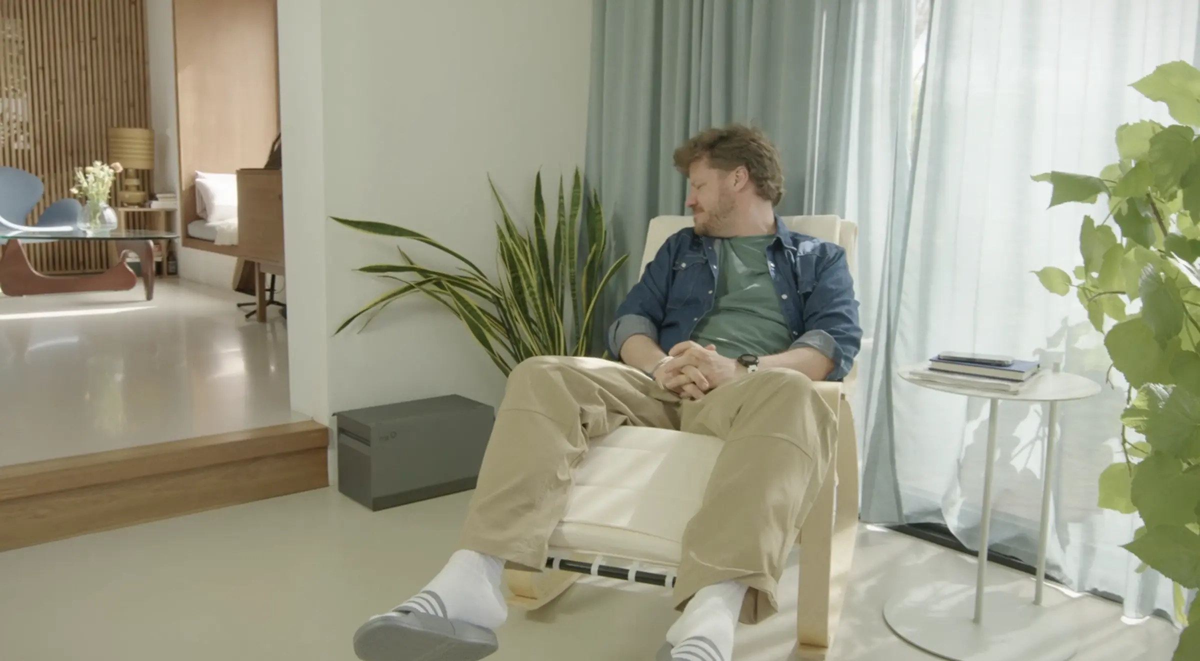 Een man zit in een luie stoel in zijn woonkamer en kijkt blij naar een plug-in thuisbatterij op de vloer.