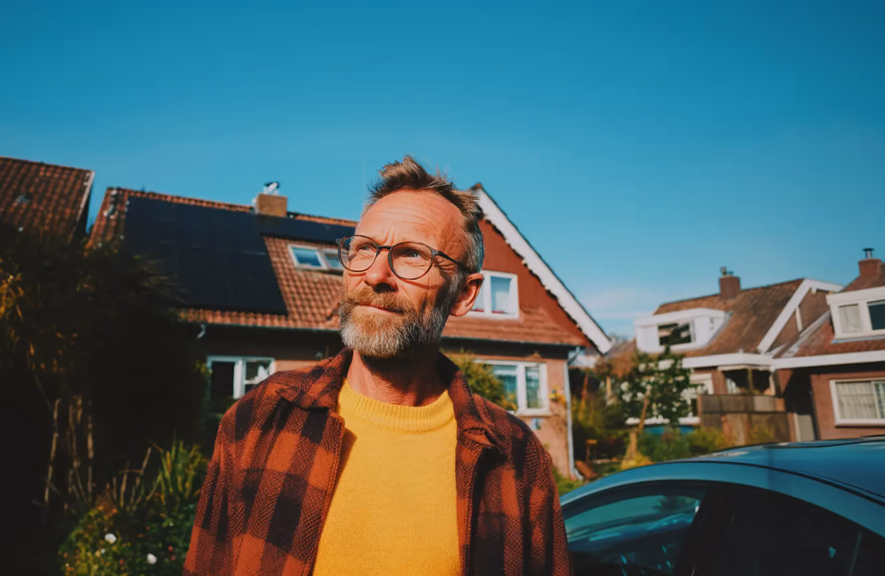 Een man in een geel shirt met rood-zwart geruit overhemd kijkt omhoog, met de zon op zijn gezicht.