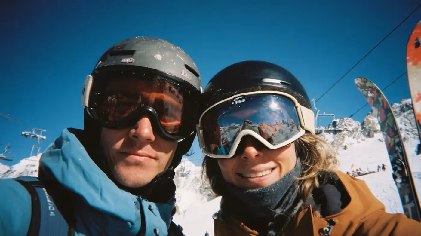 Een man en een vrouw in besneeuwde bergen, met ski-helmen en brillen op.
