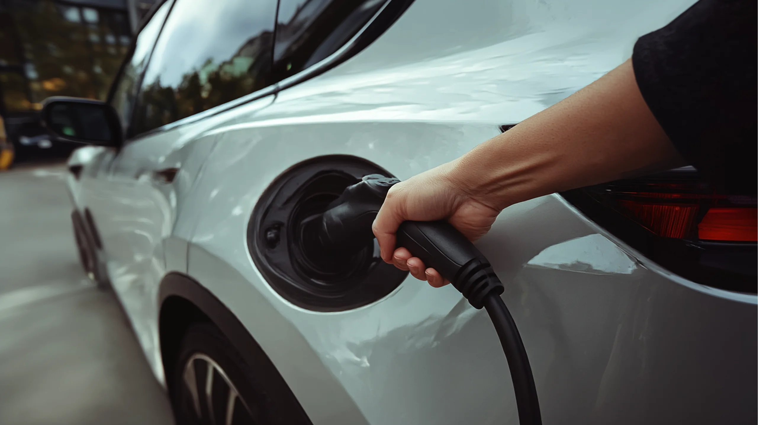 Een hand steekt een lader in de laadpoort van een witte elektrische auto.