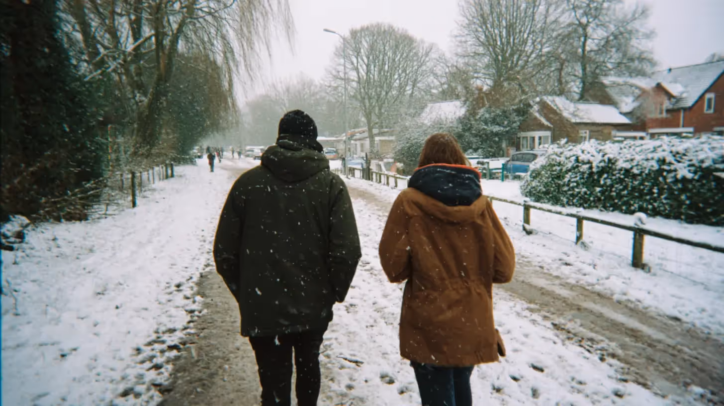 Twee mensen in winterjassen lopen door een straat in de sneeuw.