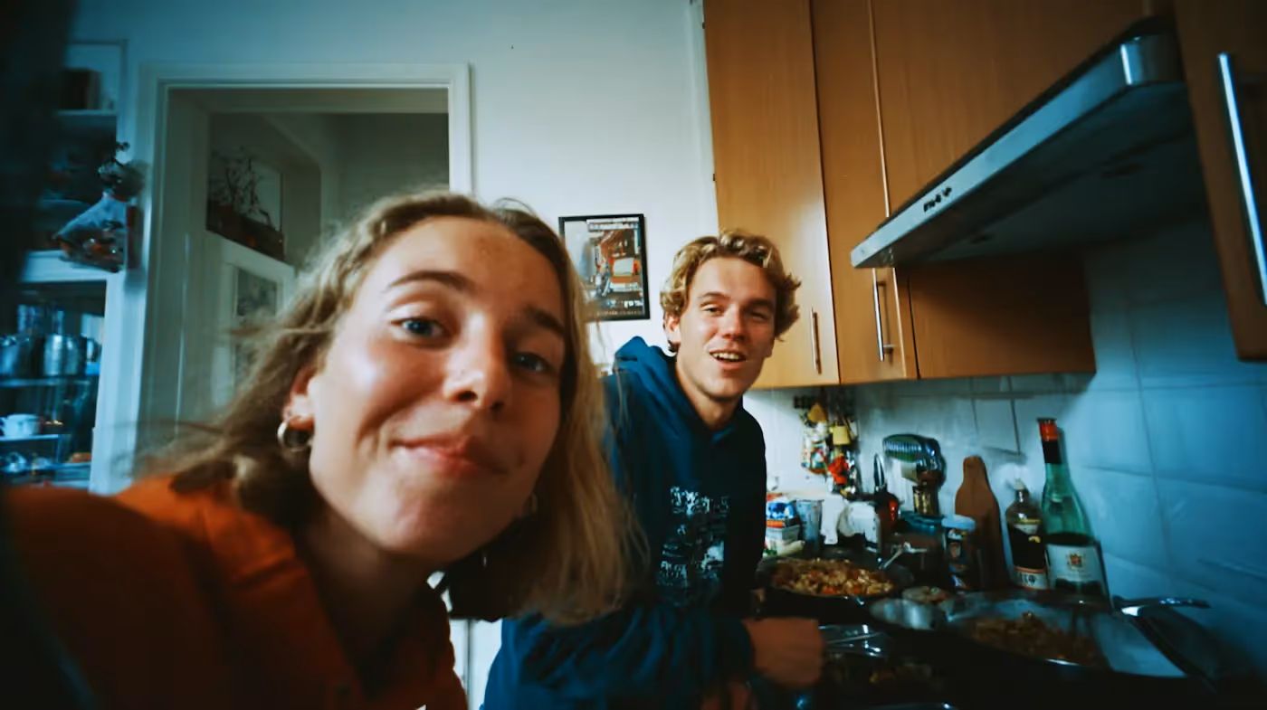 Een vrouw maakt een selfie van haarzelf en een man. Ze staan samen in de keuken.