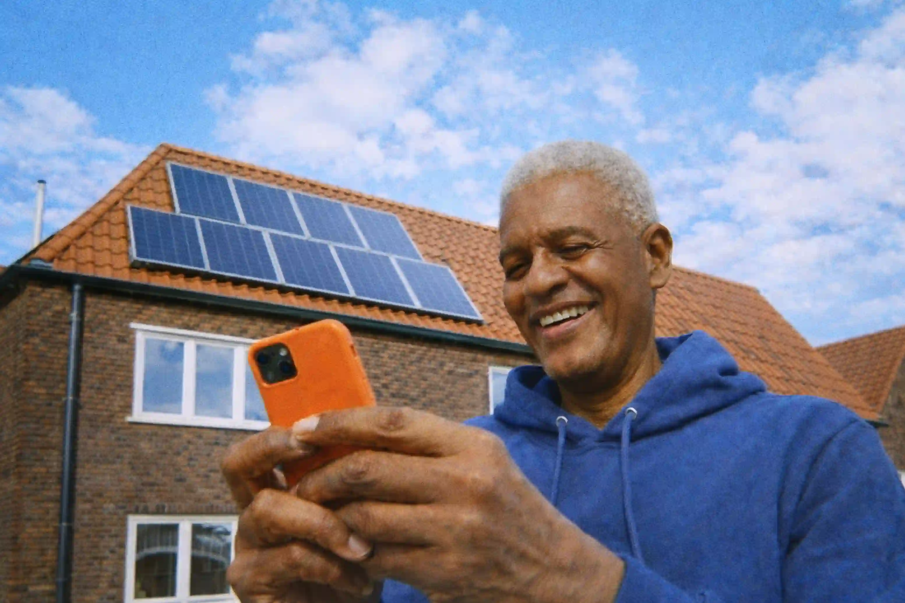 Man voor zijn huis met zonnepanelen met een mobiel in zijn hand