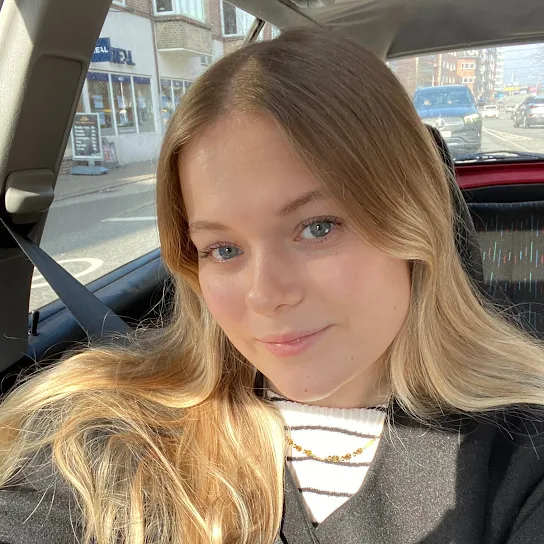 Young woman with long blonde hair wearing a seatbelt and smiling inside a car.