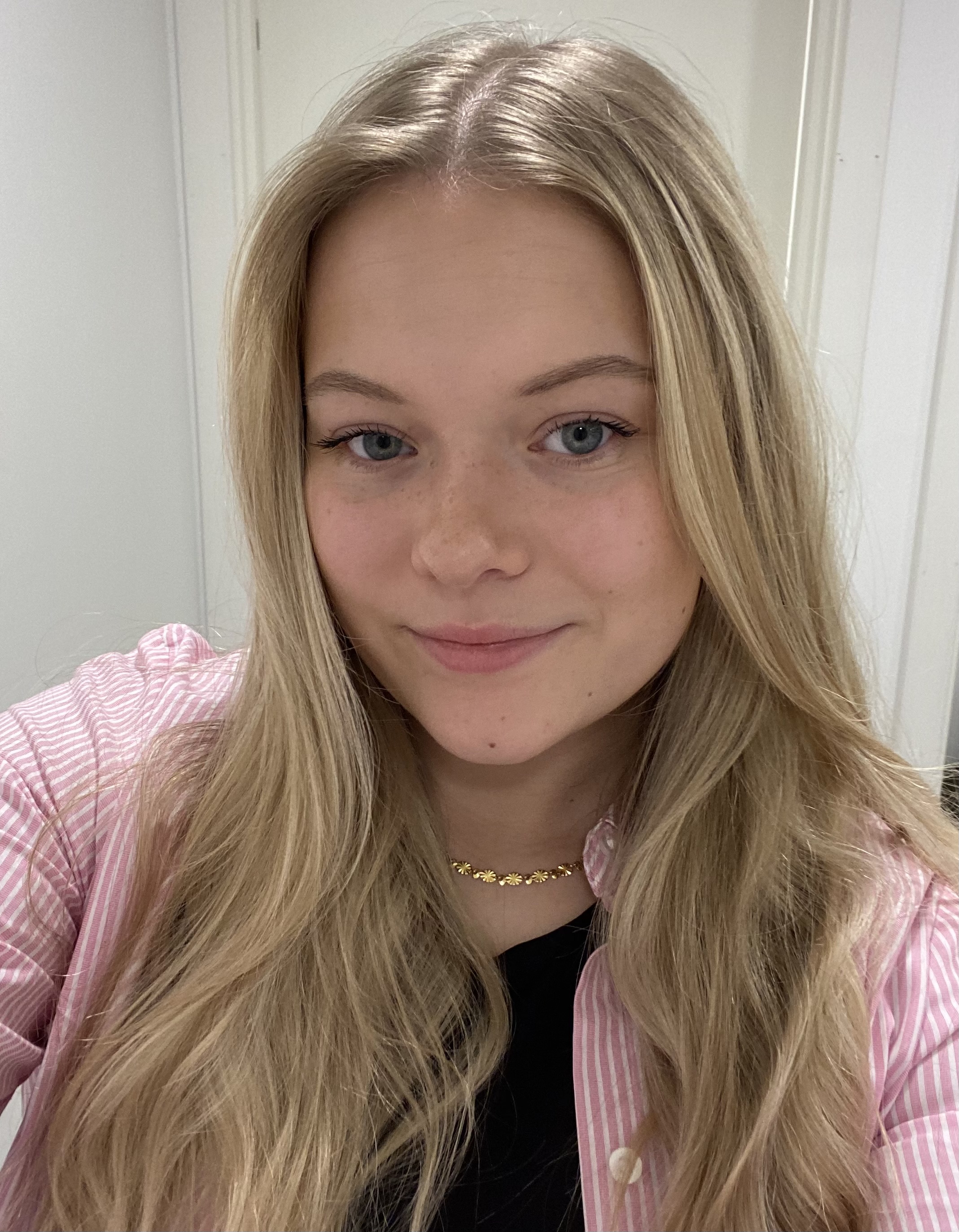 Young woman with long blonde hair wearing a seatbelt and smiling inside a car.