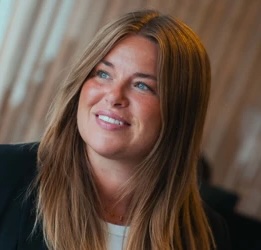 Smiling woman with long light brown hair looking slightly to the side in a softly lit indoor setting.