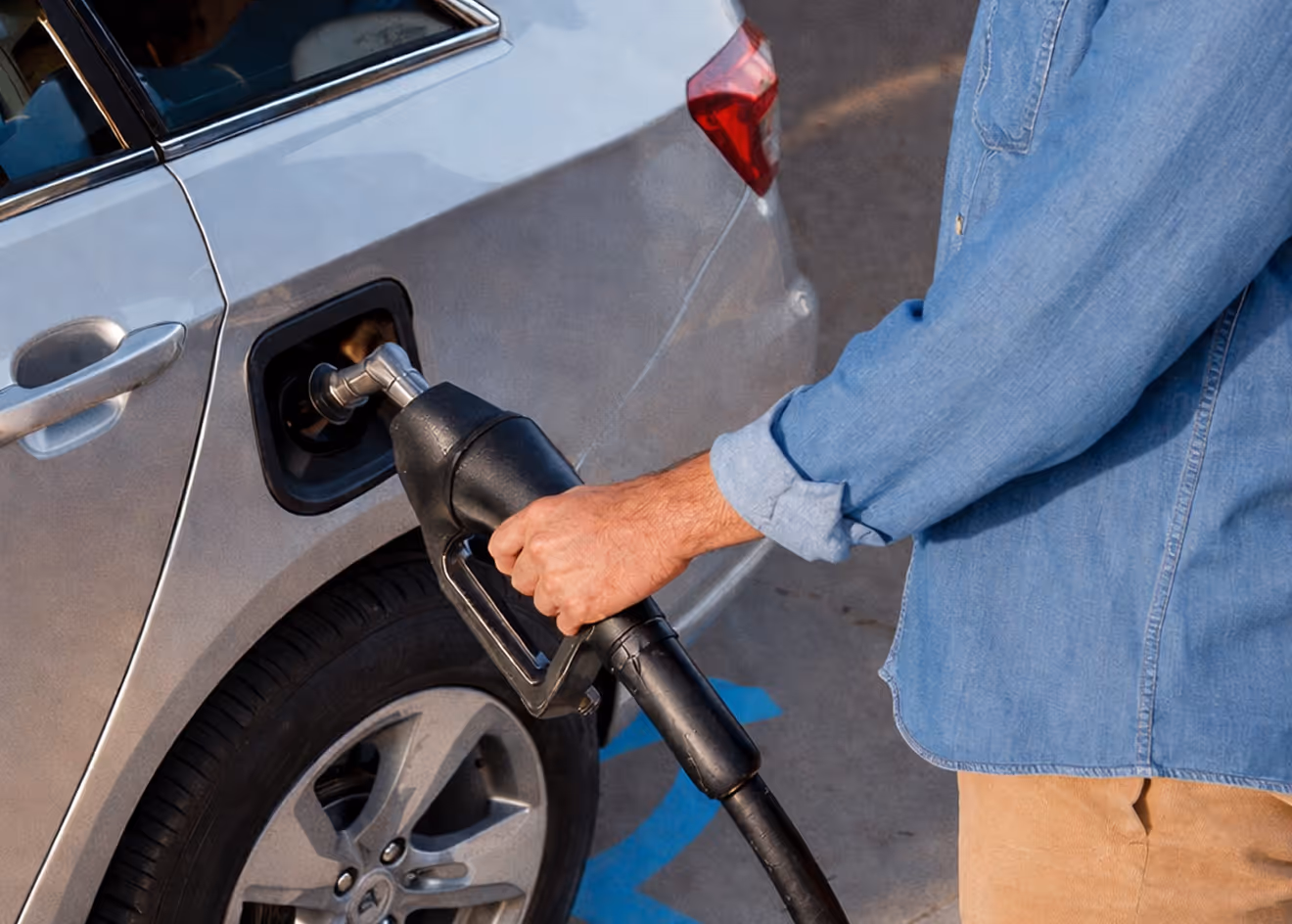 Person holding a fuel nozzle while filling a car at a gas station, with the pump inserted into the vehicle. The close view captures the action of refueling during a routine stop.