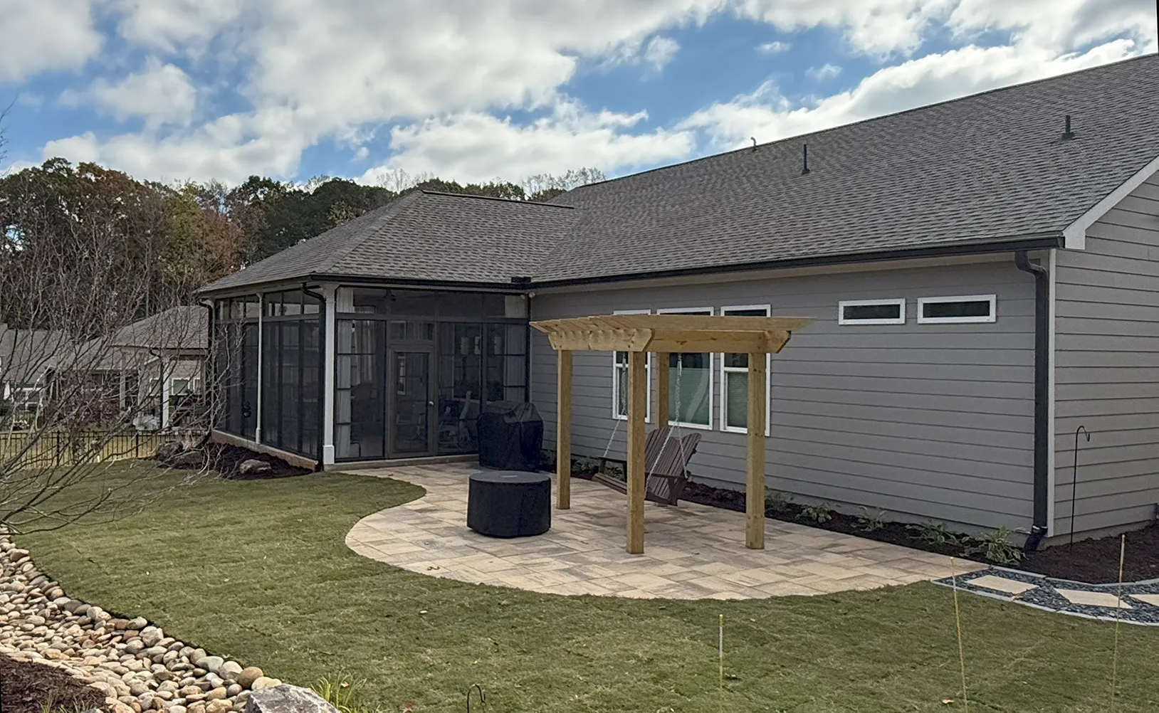 A house with a large sunroom surrounded with a patio, landscaping, and a swing.