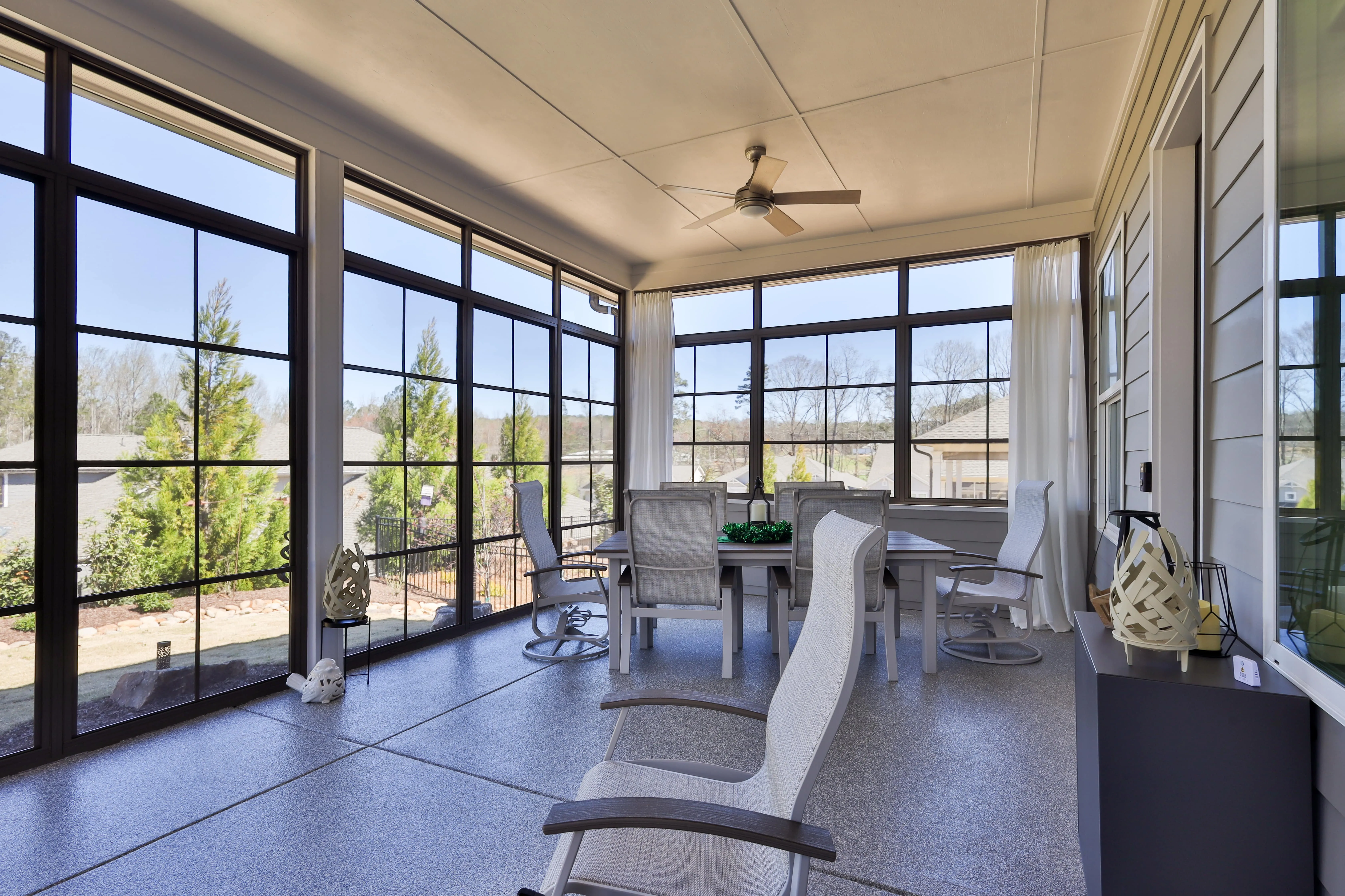 Screened-in porch with gray patio chairs around a rectangular dining table and a ceiling fan overhead.