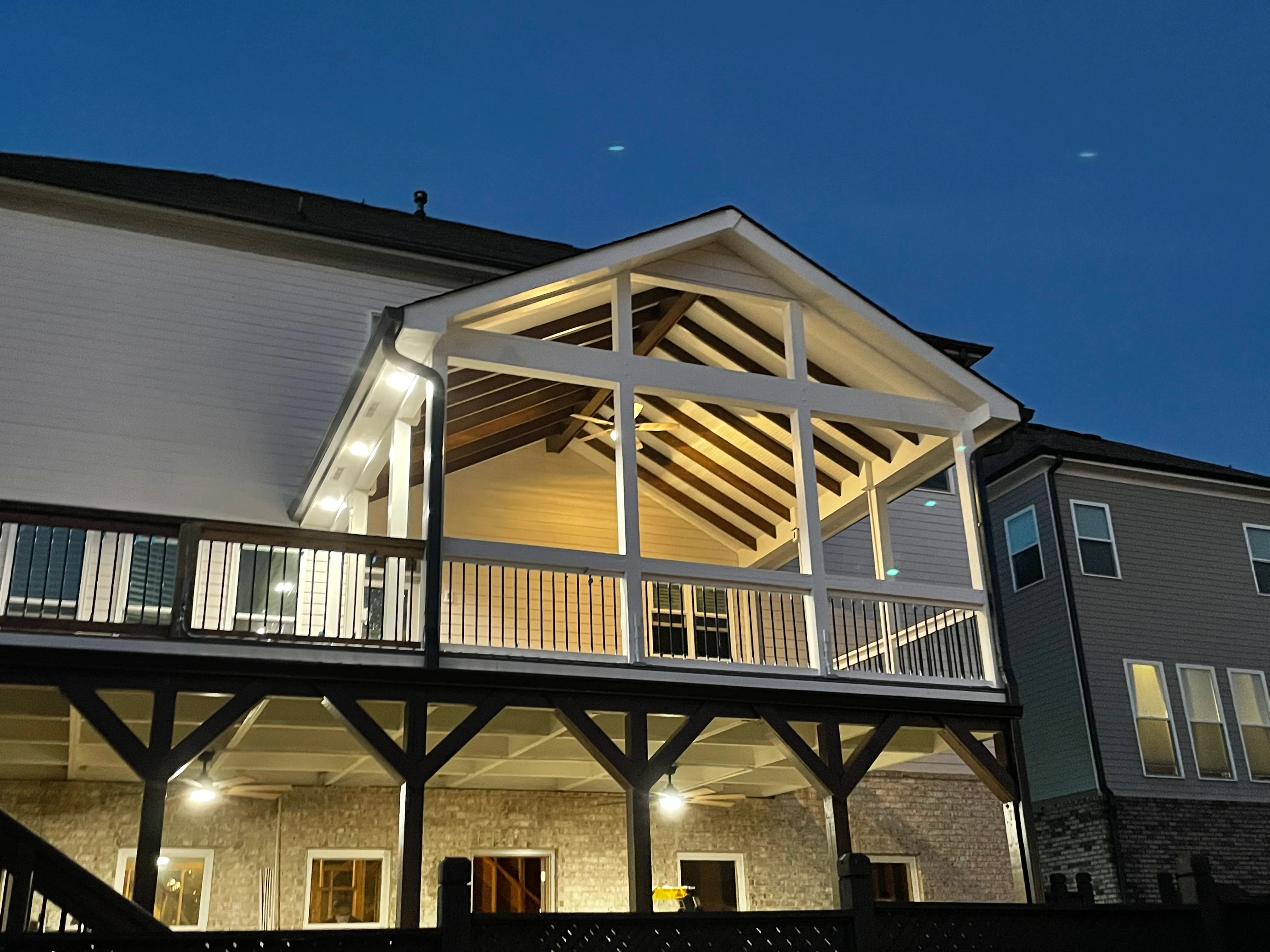 Elevated house deck with white wooden frame and exposed beams, illuminated at dusk.