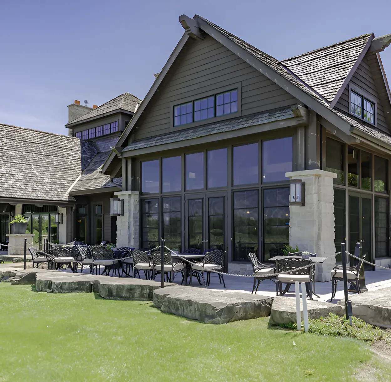 Outdoor patio seating with black metal chairs and tables in front of a large modern lodge with stone pillars and wood siding.