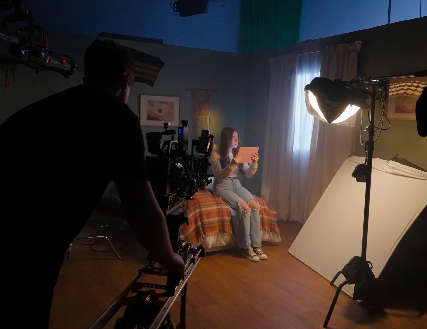 Crew set up a softbox light and camera slider around a woman seated in a dimly lit studio.