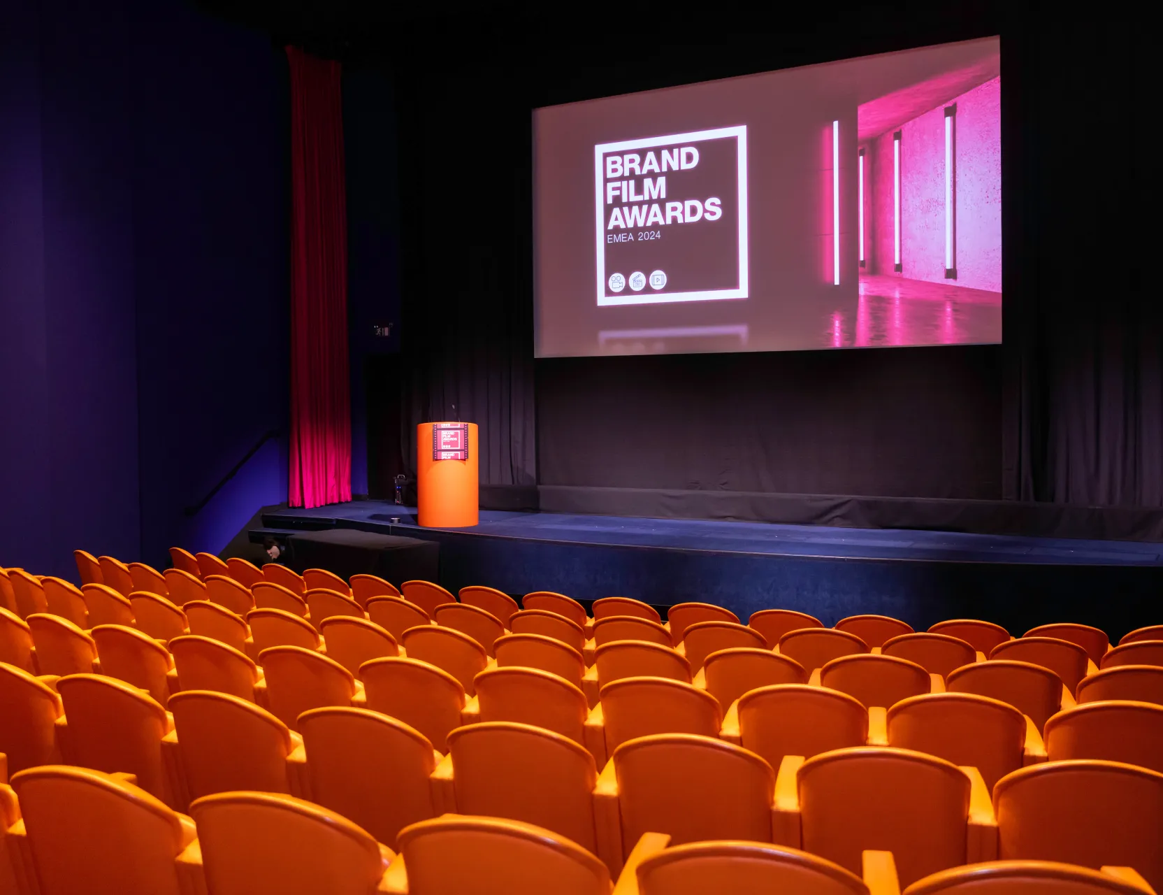 Empty cinema auditorium with orange seating and a screen displaying the Brand Film Awards EMEA 2024 title.