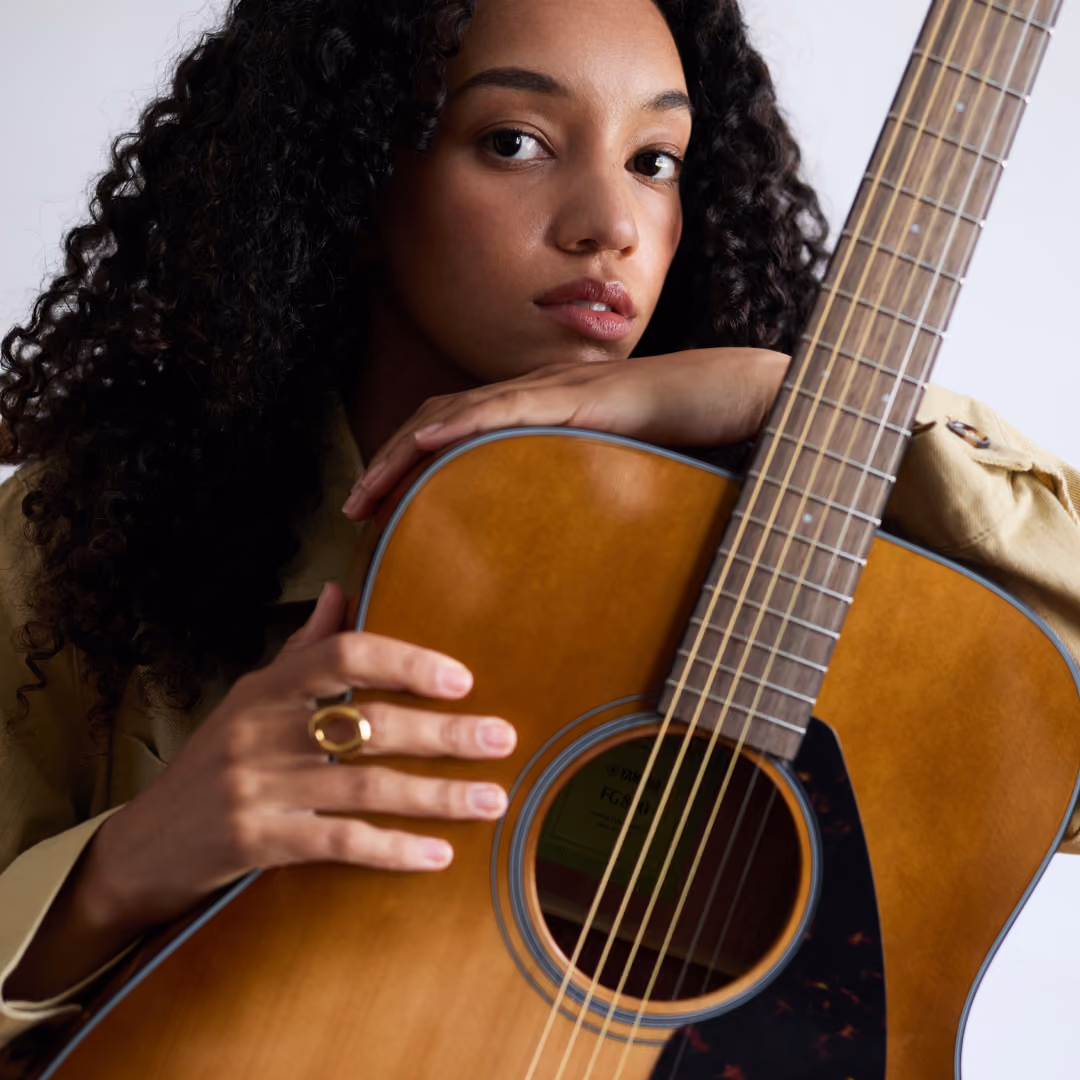 Studio portrait of a woman with curly hair resting her chin on an acoustic guitar.