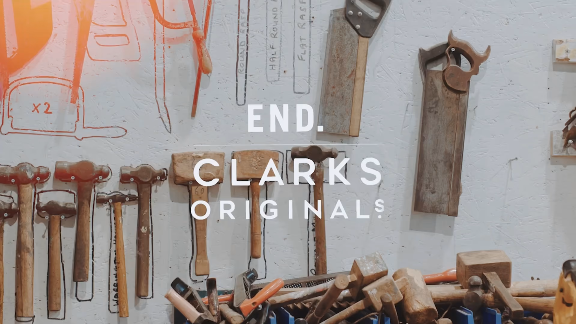A workshop wall with various hand tools such as hammers and saws hanging and placed below, overlaid with the text 'END. CLARKS ORIGINALS'.