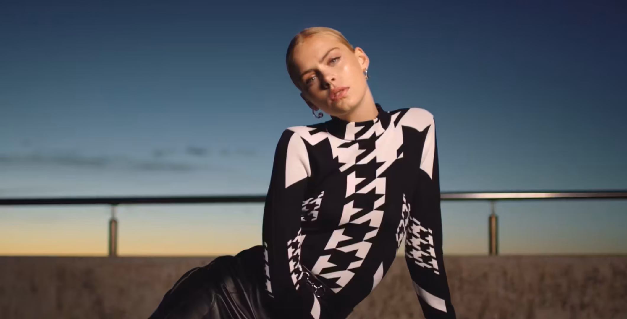 Model wearing a black and white houndstooth knit outfit, photographed outdoors against a dusk sky, from a Karen Millen campaign