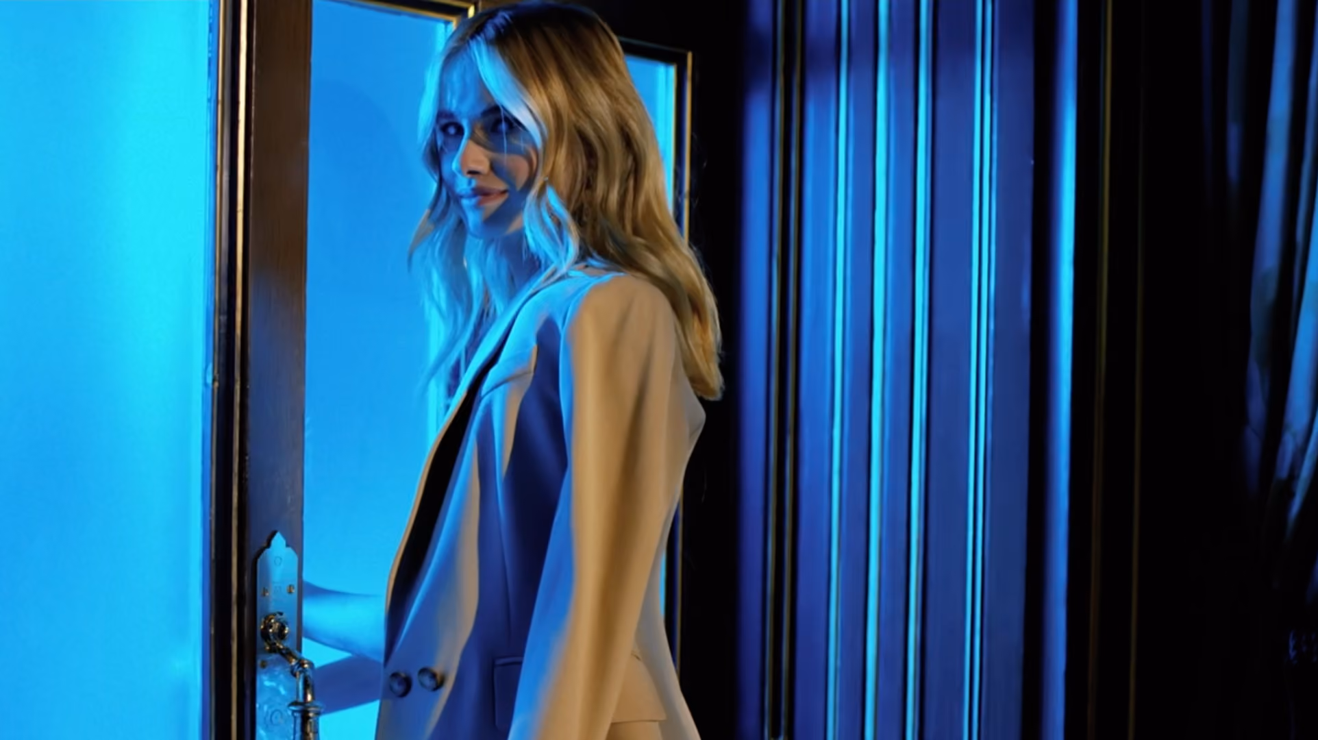 Model in a beige blazer walking through a blue-lit doorway at night, from a Karen Millen campaign