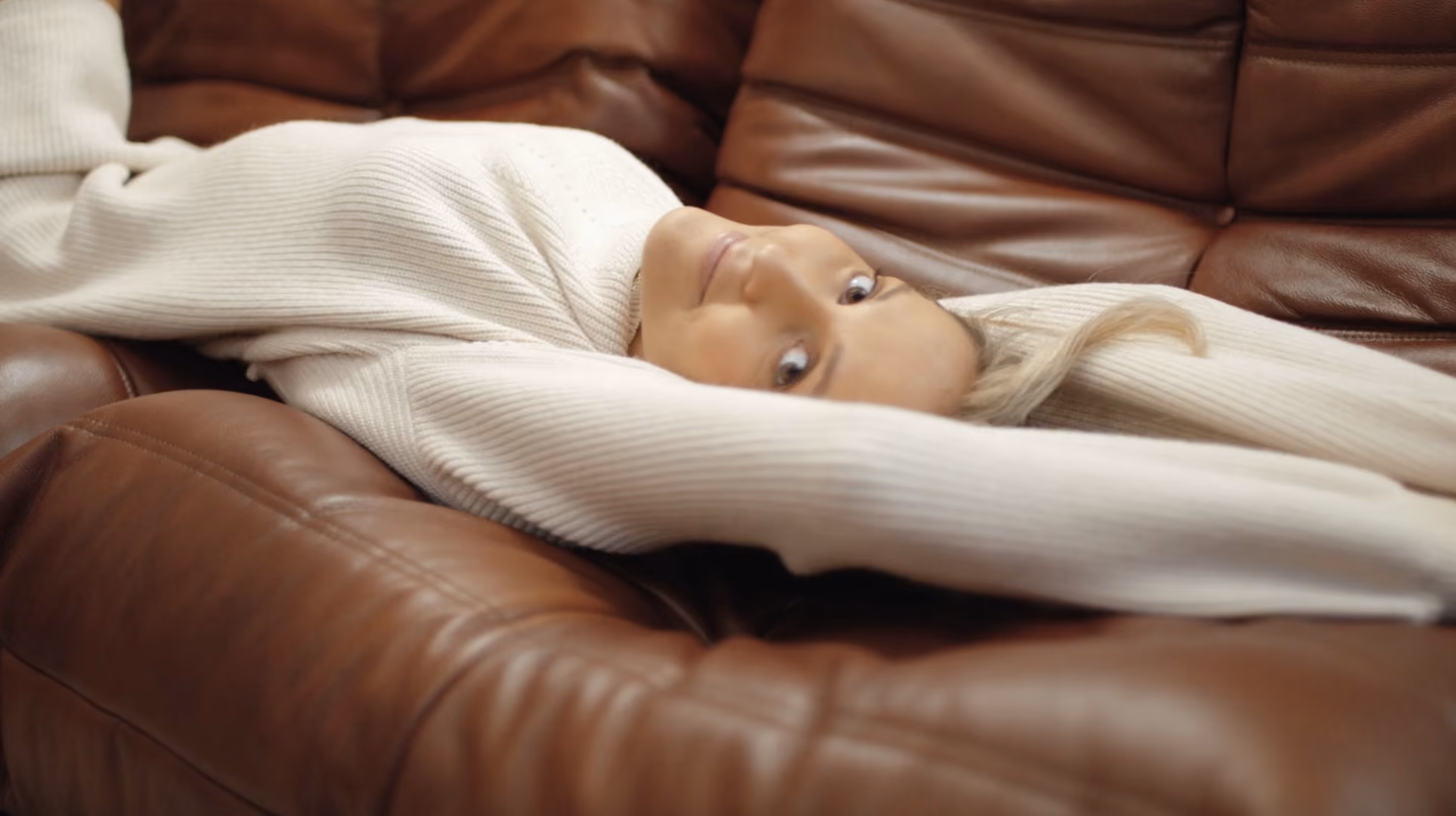 Baby wrapped in a white knitted blanket lying on a brown leather sofa, from a 4th & Reckless campaign