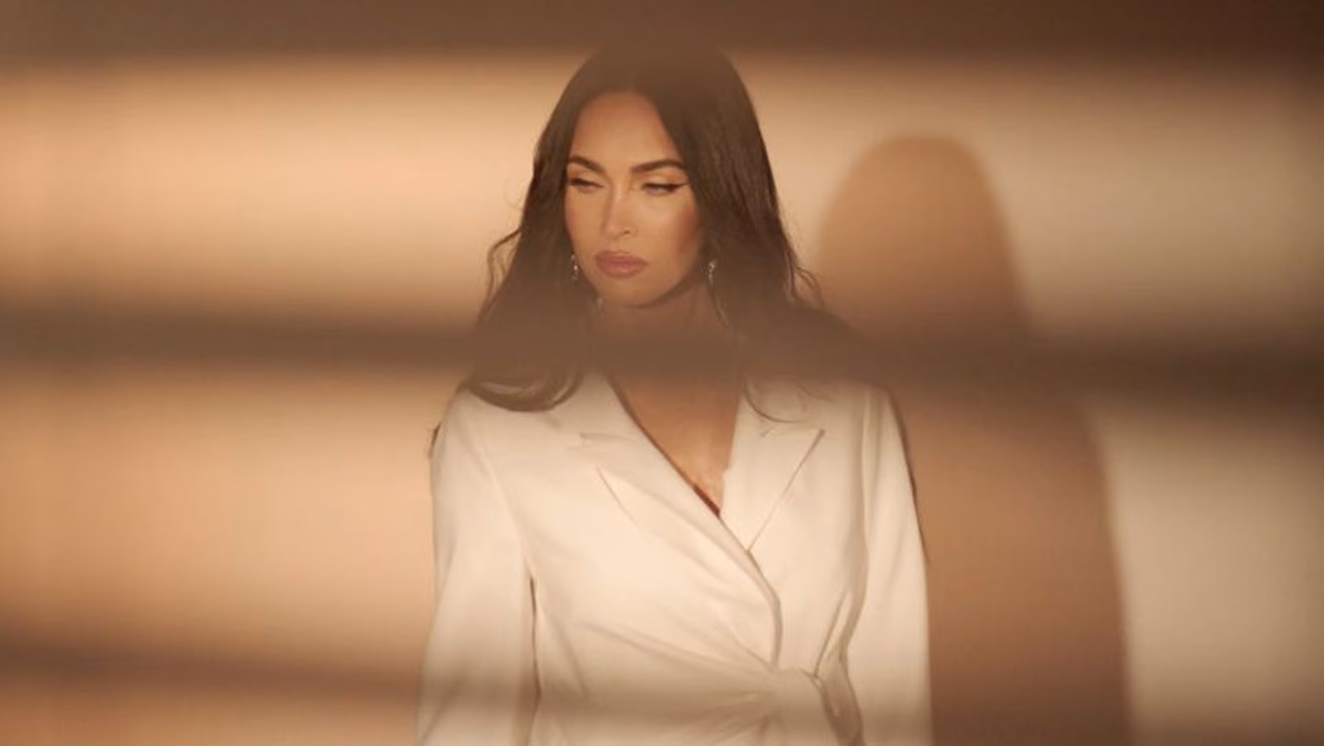 Model in a white blazer dress, softly lit with a blurred blind pattern in the foreground, from a Boohoo campaign