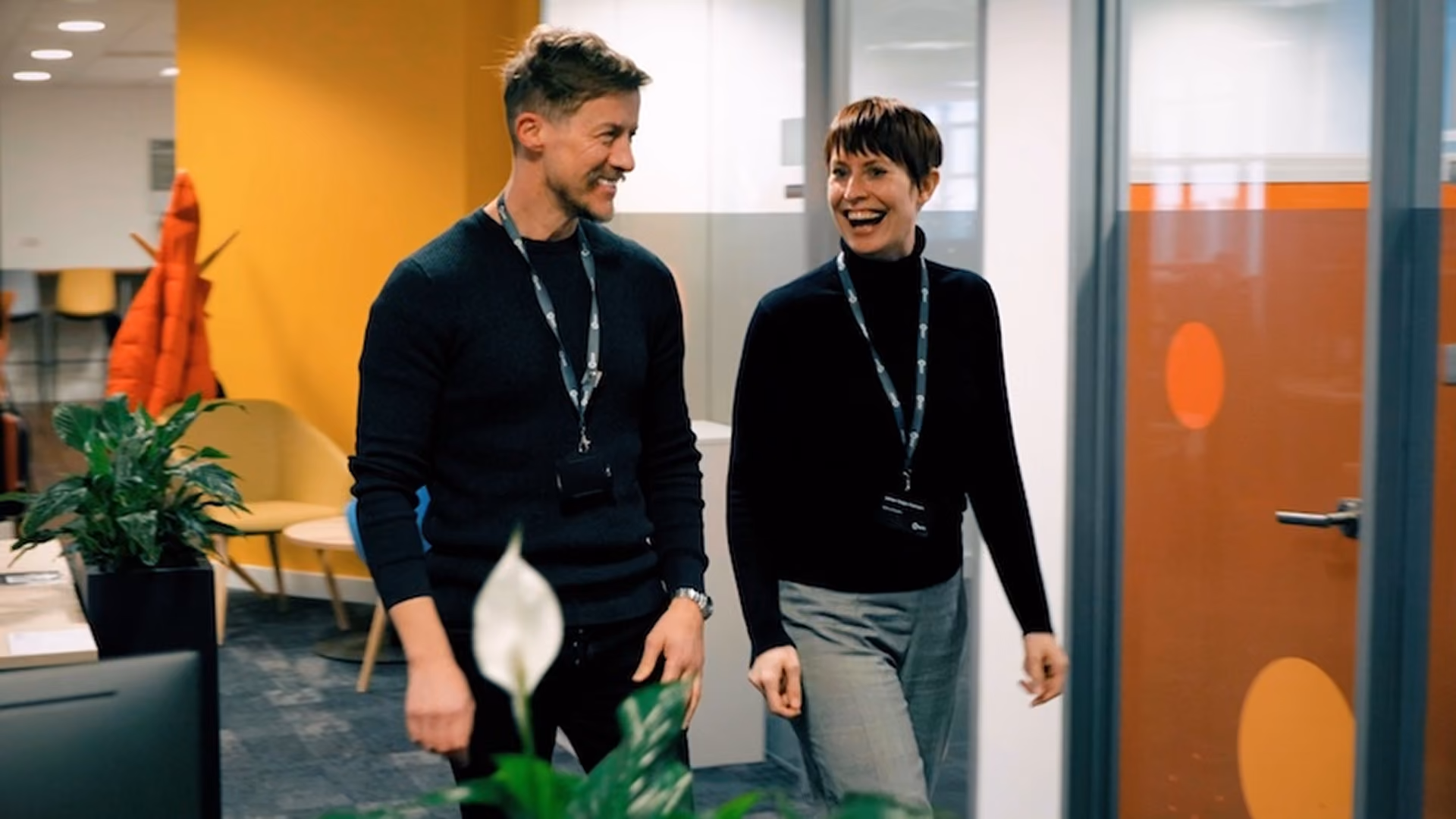Two colleagues laughing together while walking through a modern office