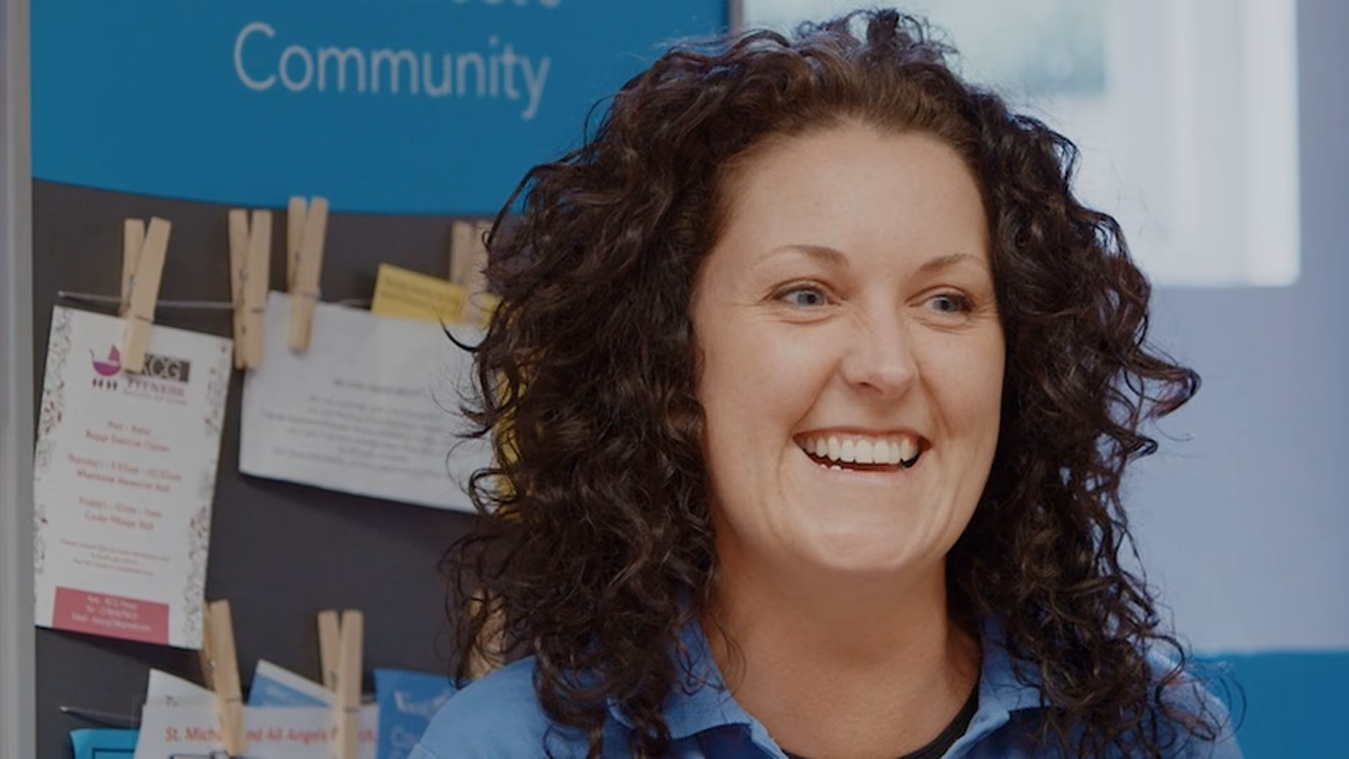 Smiling woman being interviewed in front of a community noticeboard