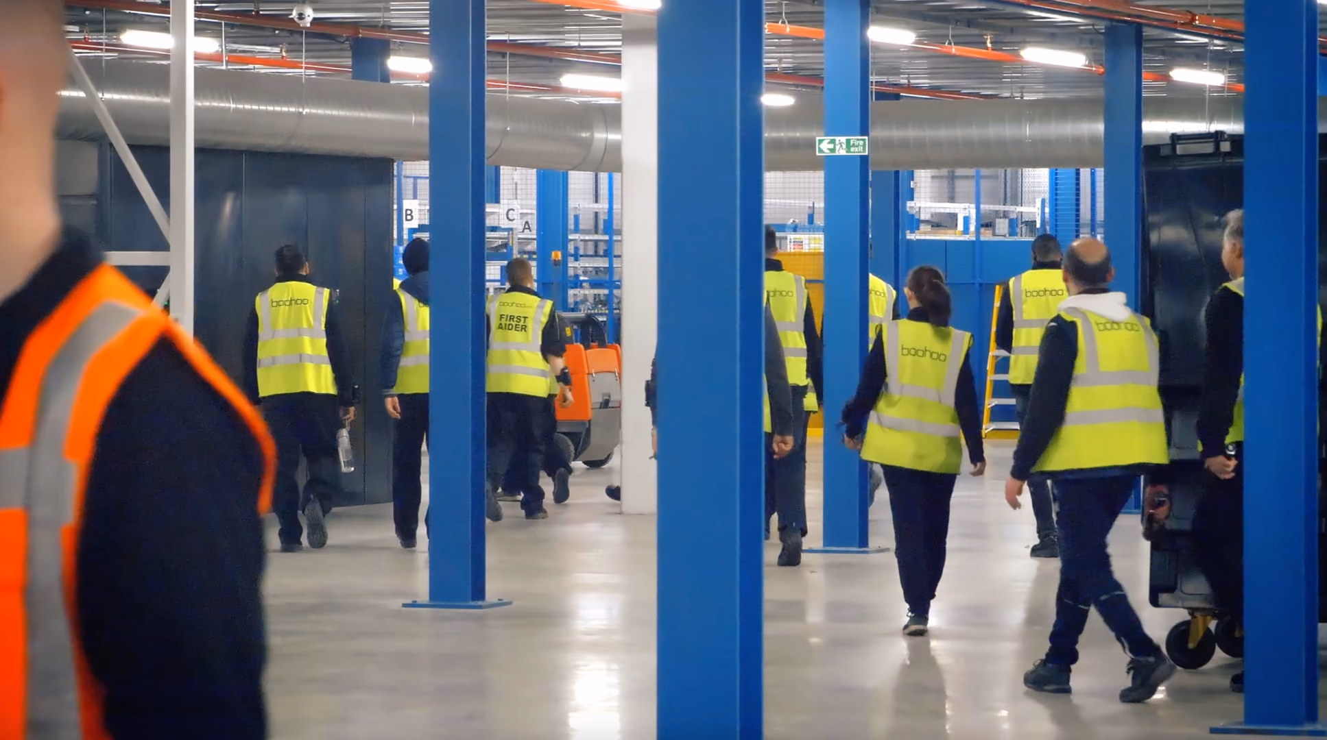 Staff in high-visibility vests walking through a warehouse, from a Boohoo campaign
