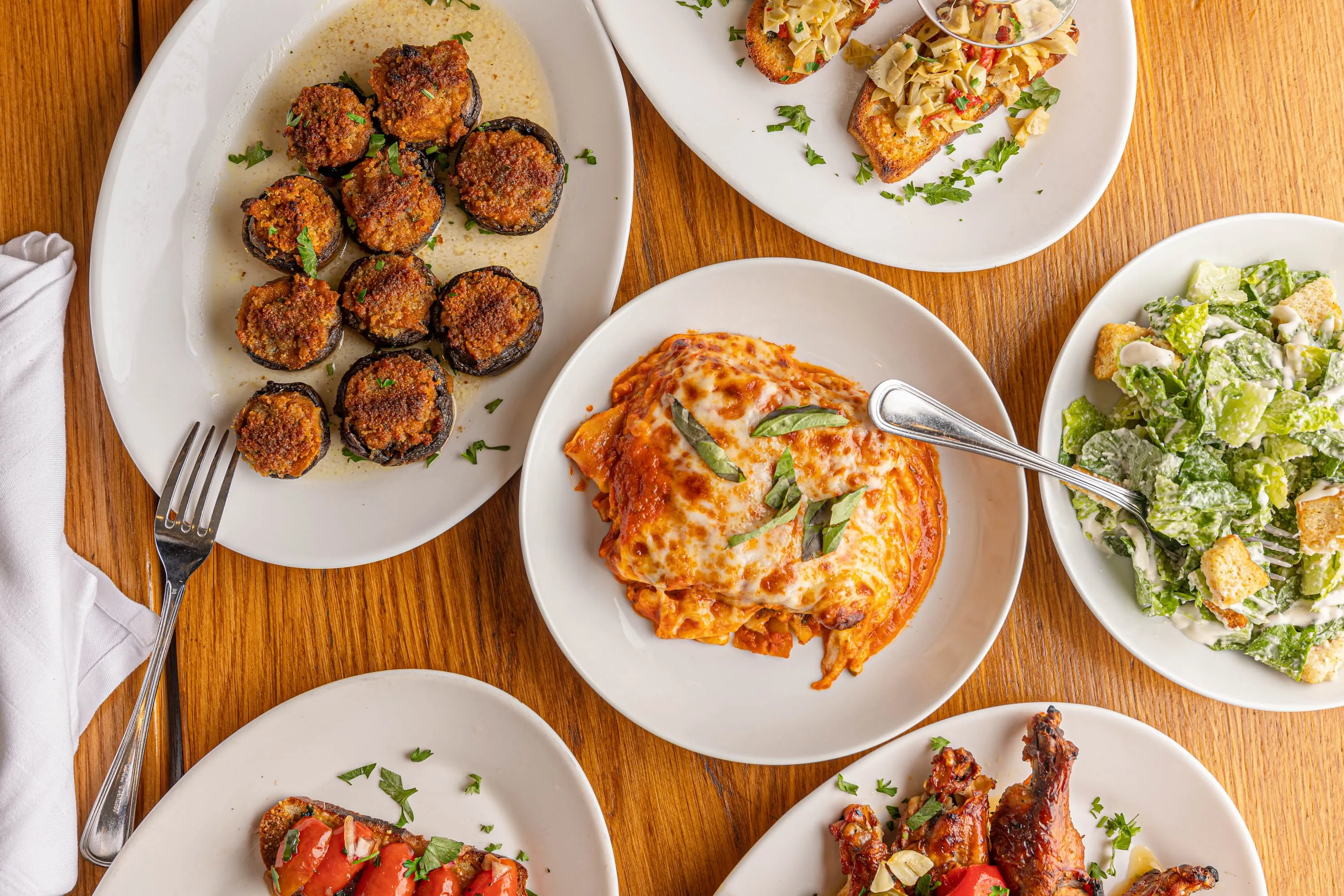 Overhead of shared Italian plates at Adrienne's Pizzabar, including baked pasta, stuffed mushrooms, salad, and toasted bread