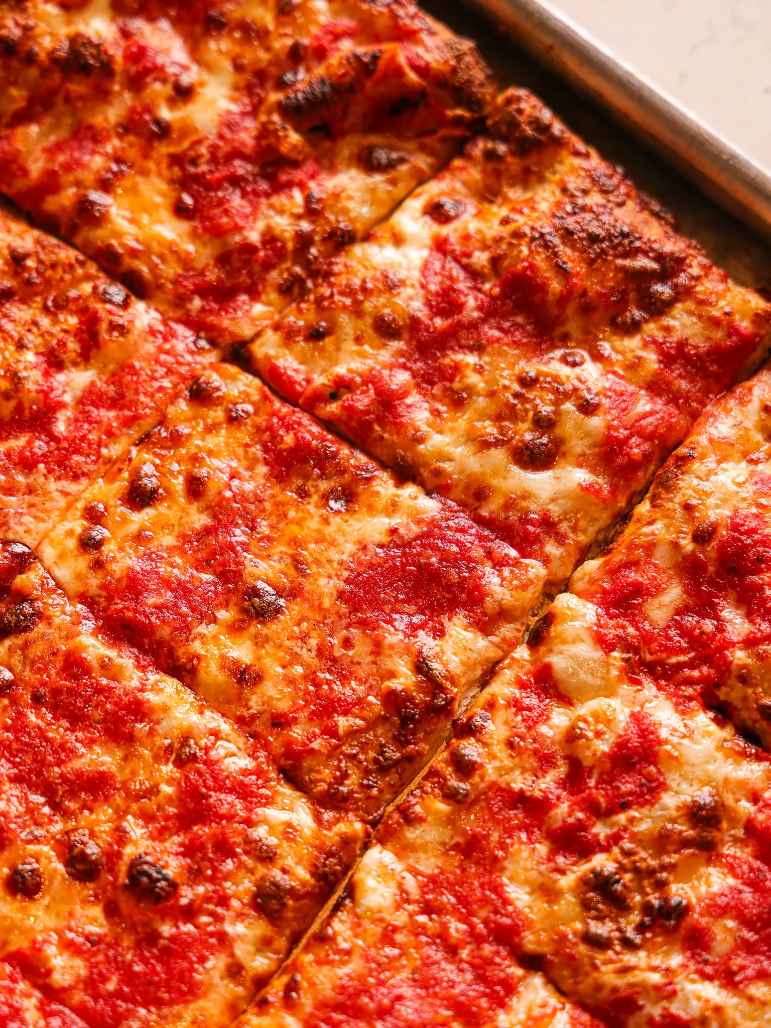 Four trays of rectangular pizzas with various toppings including mushrooms, artichokes, pepperoni, red onions, sausage, arugula, and prosciutto on a wooden table.