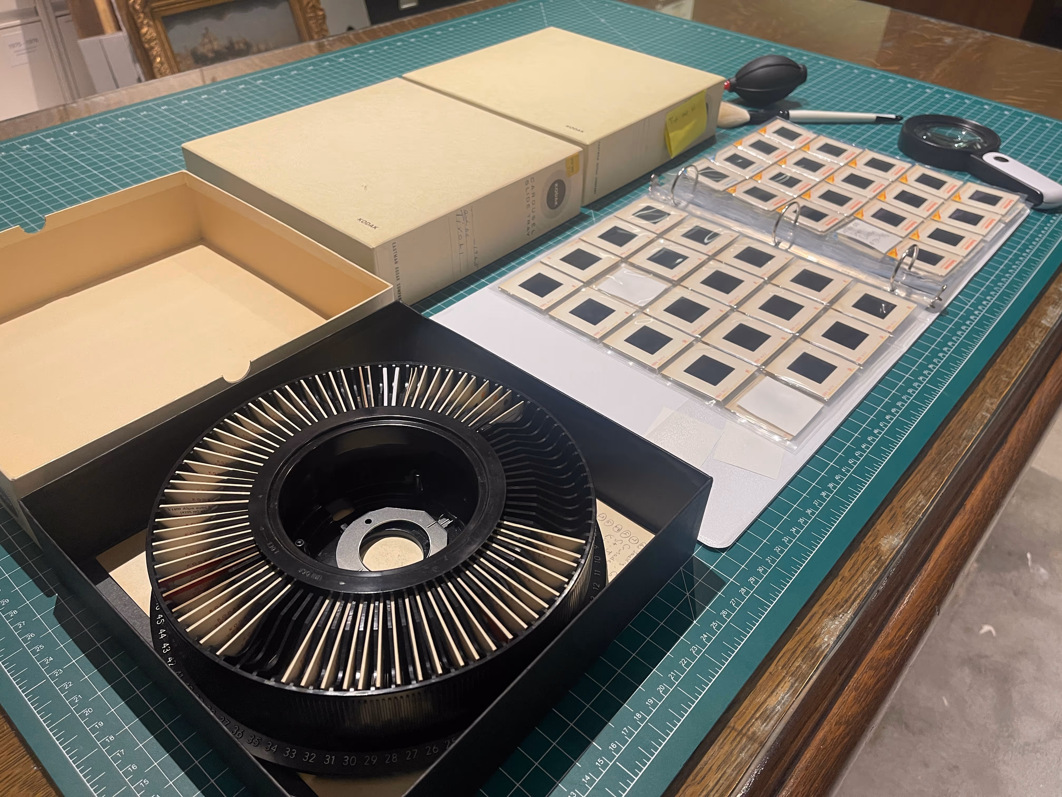 Vintage slide projector carousel with numerous slides arranged in a binder on a green cutting mat table.