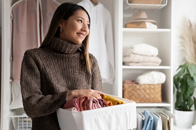 Asian woman organising clothes in a tidy wardrobe with neatly folded items on shelves