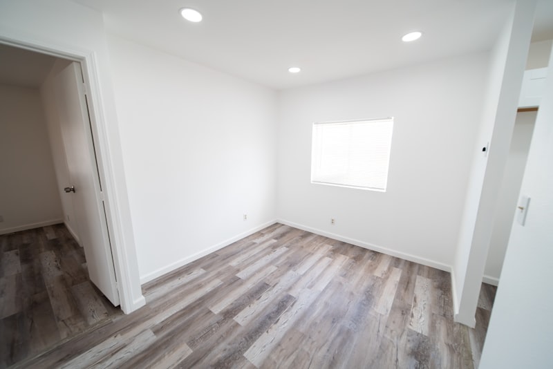Empty modern Singapore-style room with bright white walls, a wooden floor and natural daylight from a side window