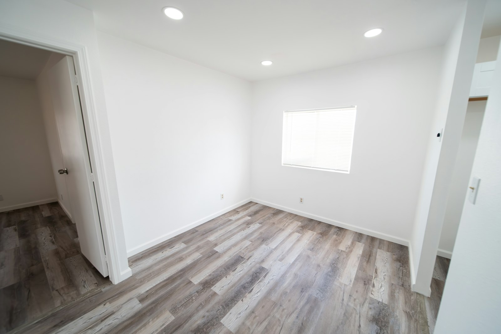 Empty modern Singapore-style room with bright white walls, a wooden floor and natural daylight from a side window