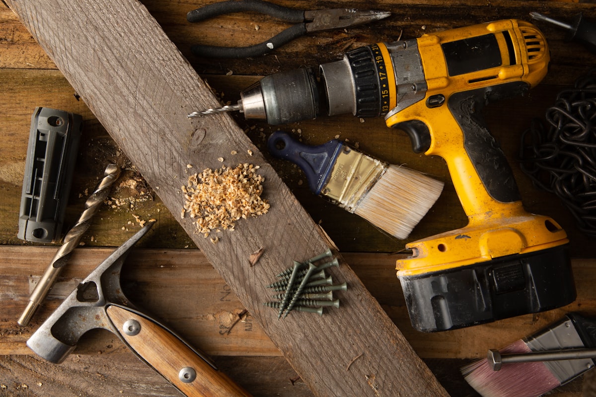 A cordless drill, screws and hand tools resting on a timber plank during a repair