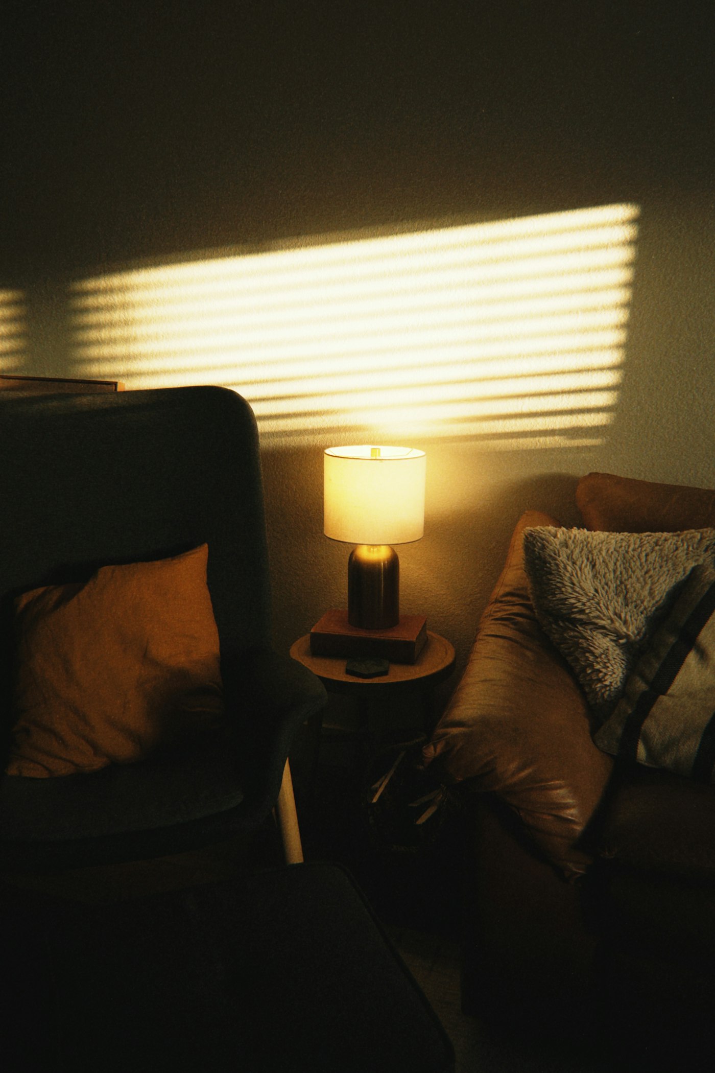 A cosy living room with armchairs, a lit lamp and soft window light