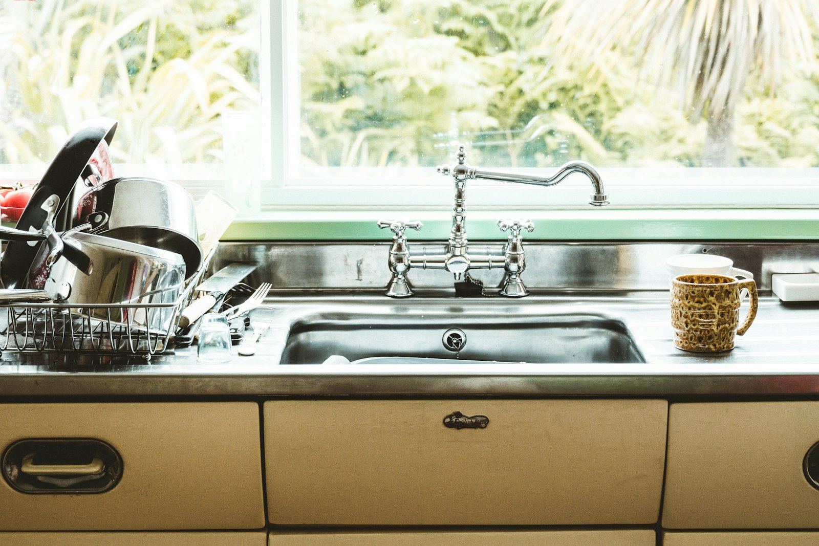 Clean stainless steel kitchen sink and dish rack beneath a bright window