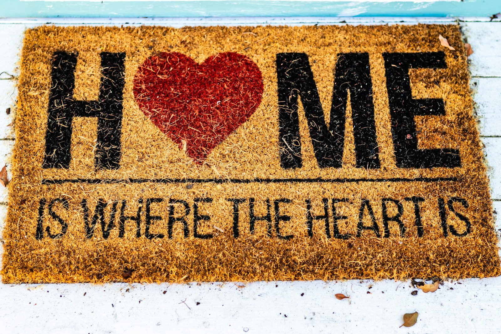 A coir door mat reading Home Is Where The Heart Is on a light floor