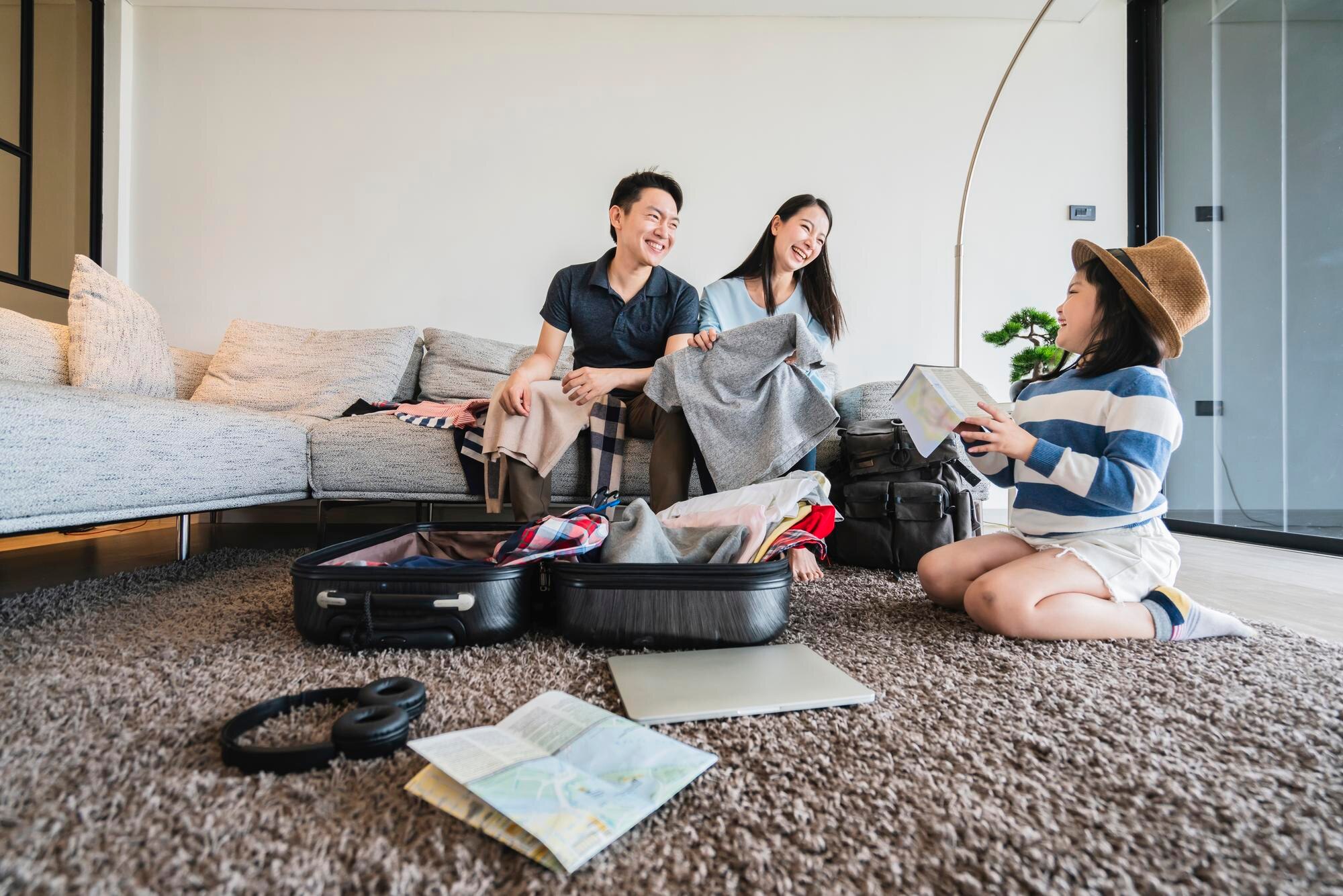 A family sitting in a bright apartment living room with open suitcases and clothes spread across the floor