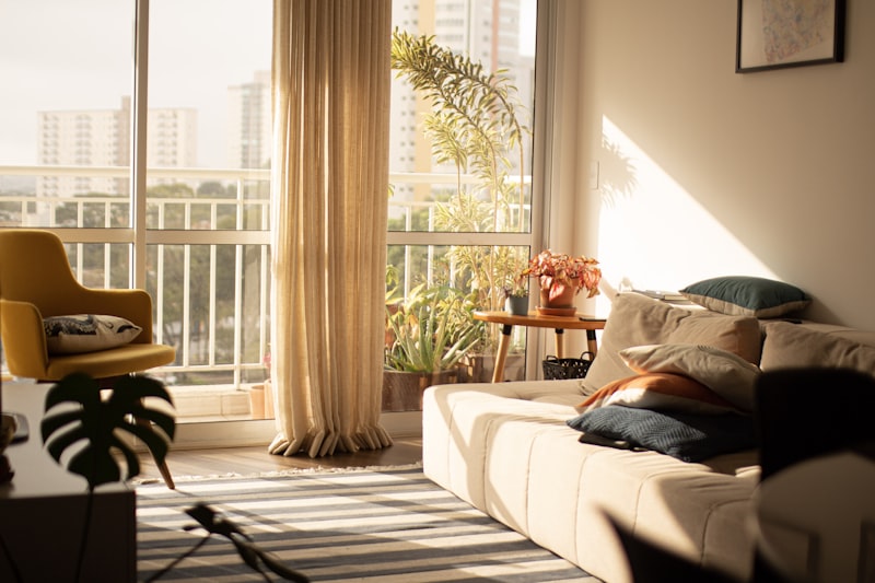 Late-afternoon sunlight filling a high-rise living room with a cream sofa, balcony plants and sheer curtains