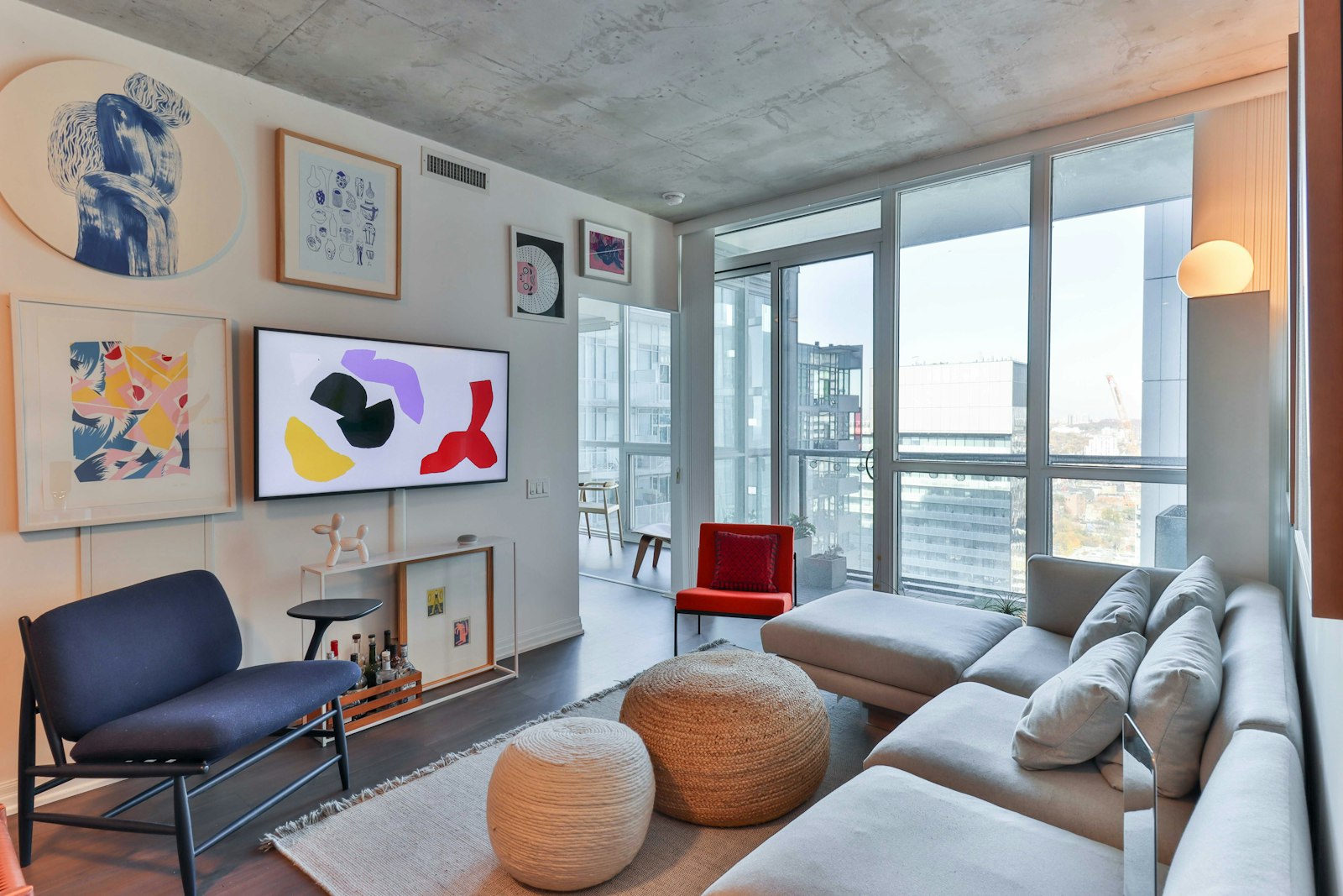 Bright condominium living room with a grey sofa, woven poufs and a city view