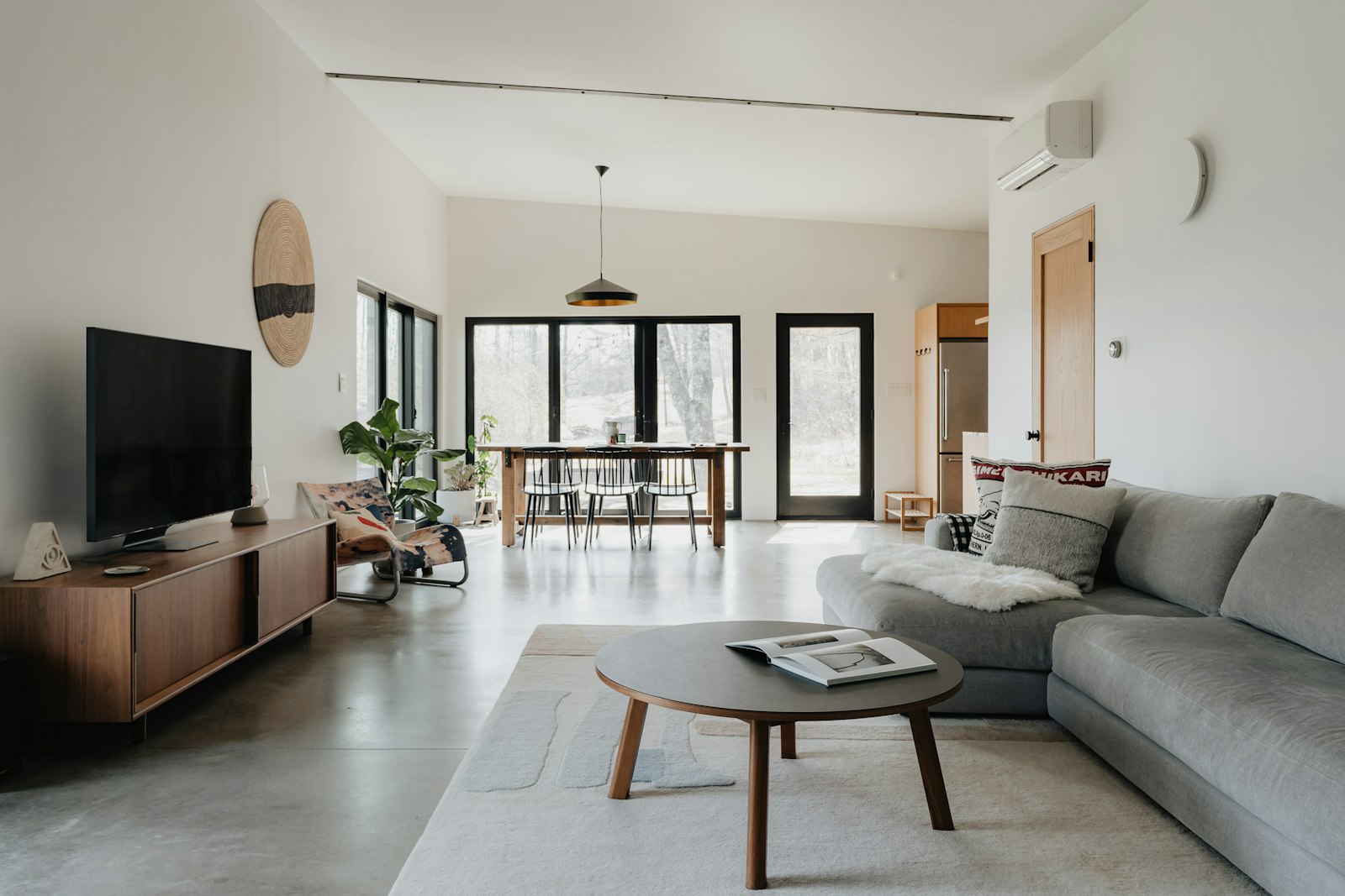 Bright open-plan living room in a modern flat with a grey sofa, wooden console and wall-mounted aircon unit