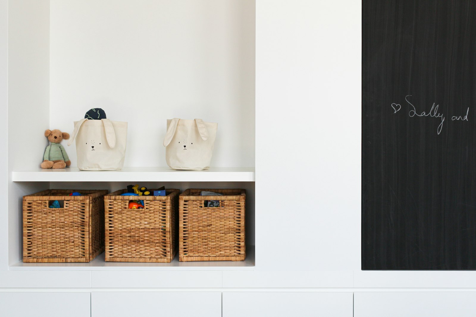 White built-in storage nook with woven baskets and cloth bags on open shelves